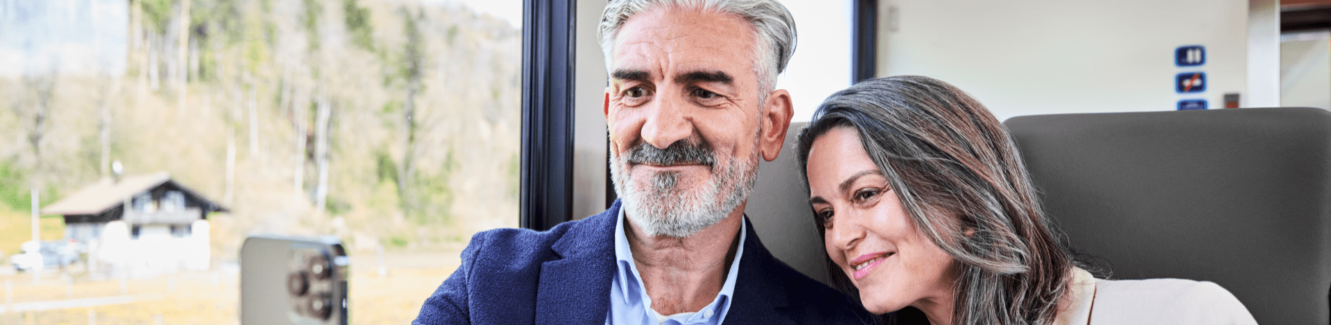 Frau und Mann sitzen in einem Zug und machen ein Selfie mit dem Smartphone.